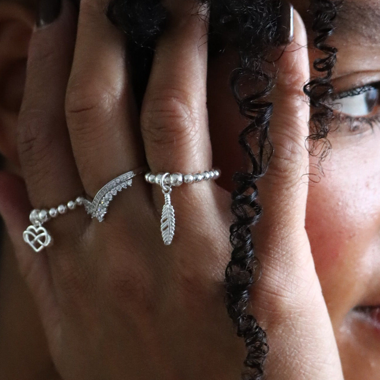 Woman with jewelry on her hand and face, wearing a white top against a dark background