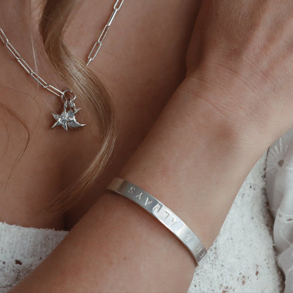 A person wearing a white shirt with a silver-colored cuff bangle on their wrist.