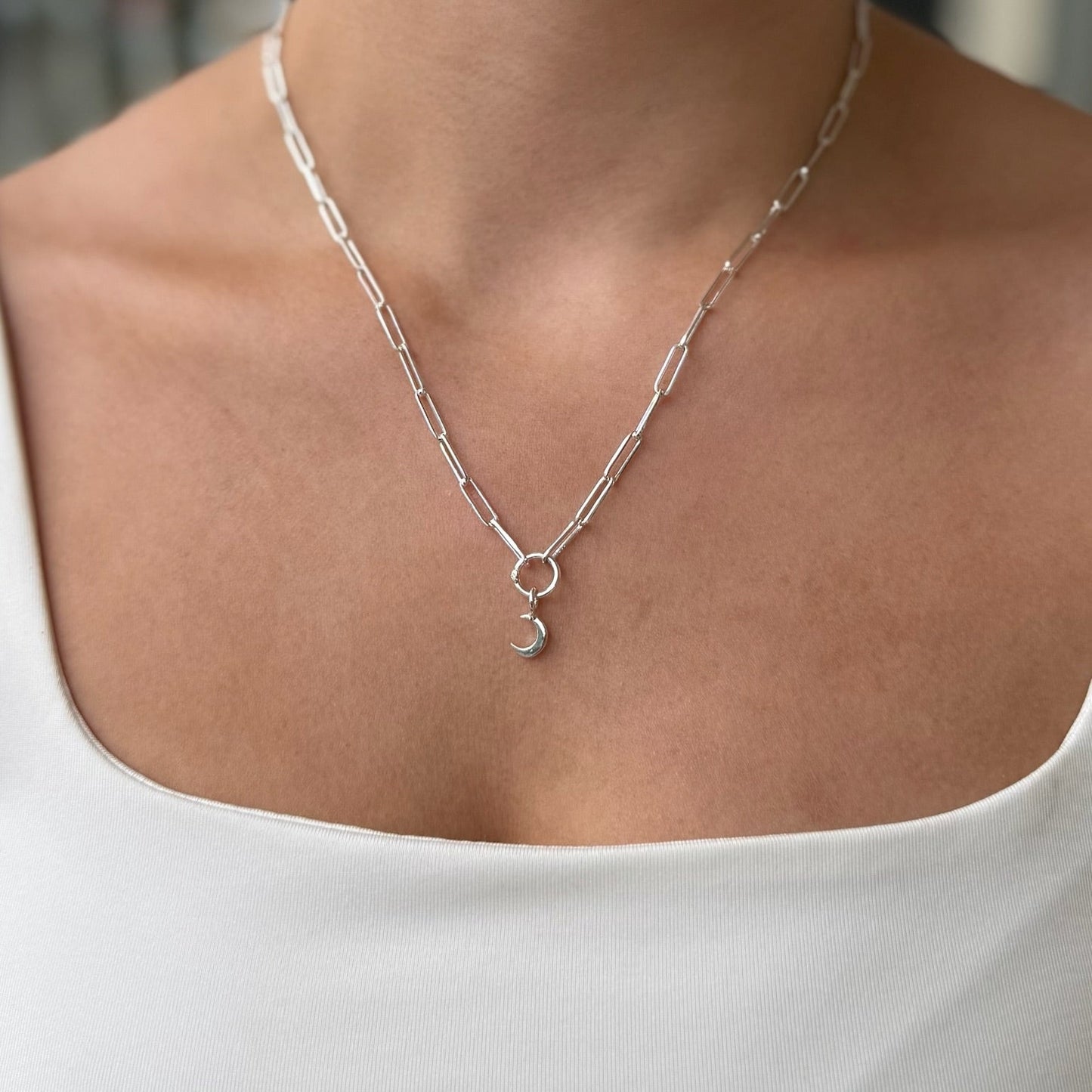 Silver necklace with a pendant worn by a person in a white top.
