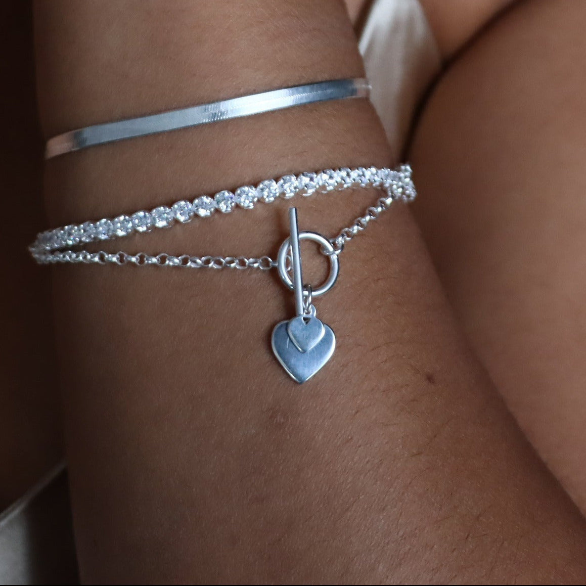 Close-up of a person wearing silver jewelry including bracelets and a necklace with heart-shaped pendants.