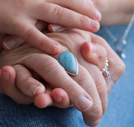 Close-up of a hand holding a child's hand with a blue stone ring.