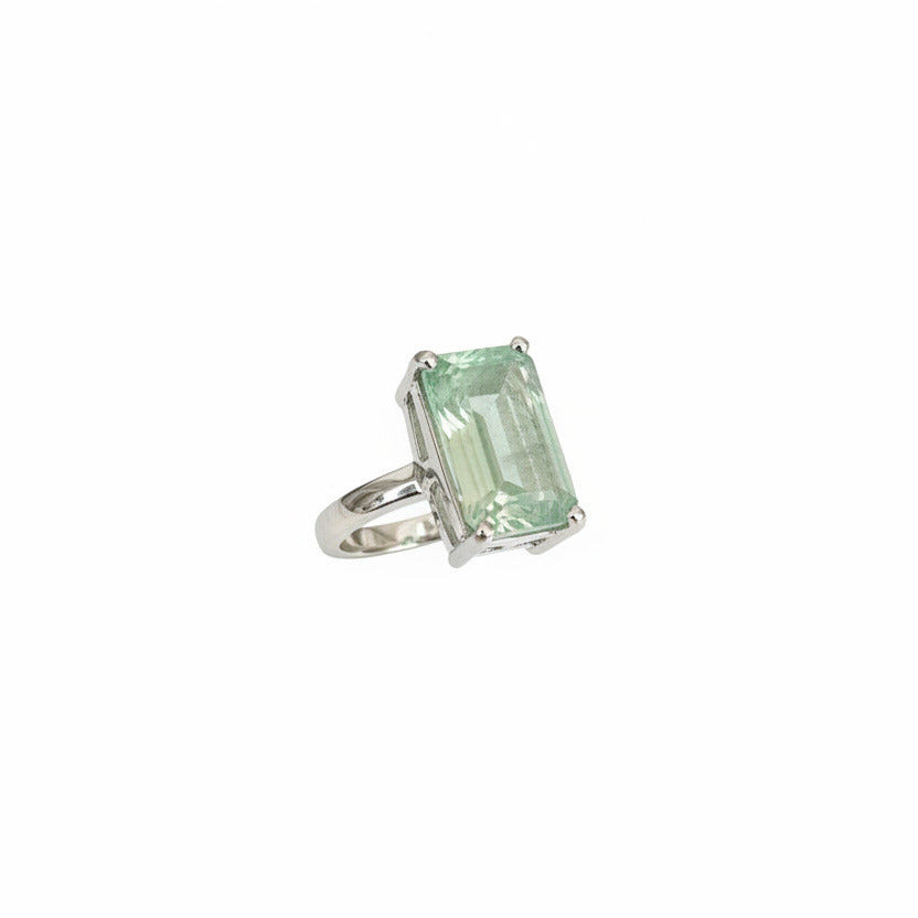 Green gemstone ring in a white box held by a hand with pink nail polish.