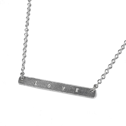 Belcher bar necklace stamped “love” on a white background 