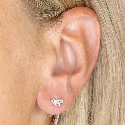 Silver bow-shaped earring worn on a person's ear.