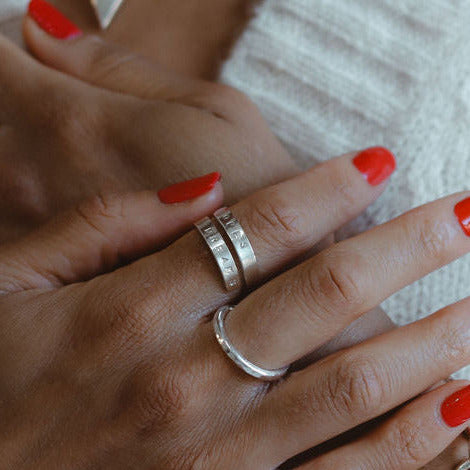 A person's hand with a silver ring on the finger, alongside a silver-colored bracelet.
