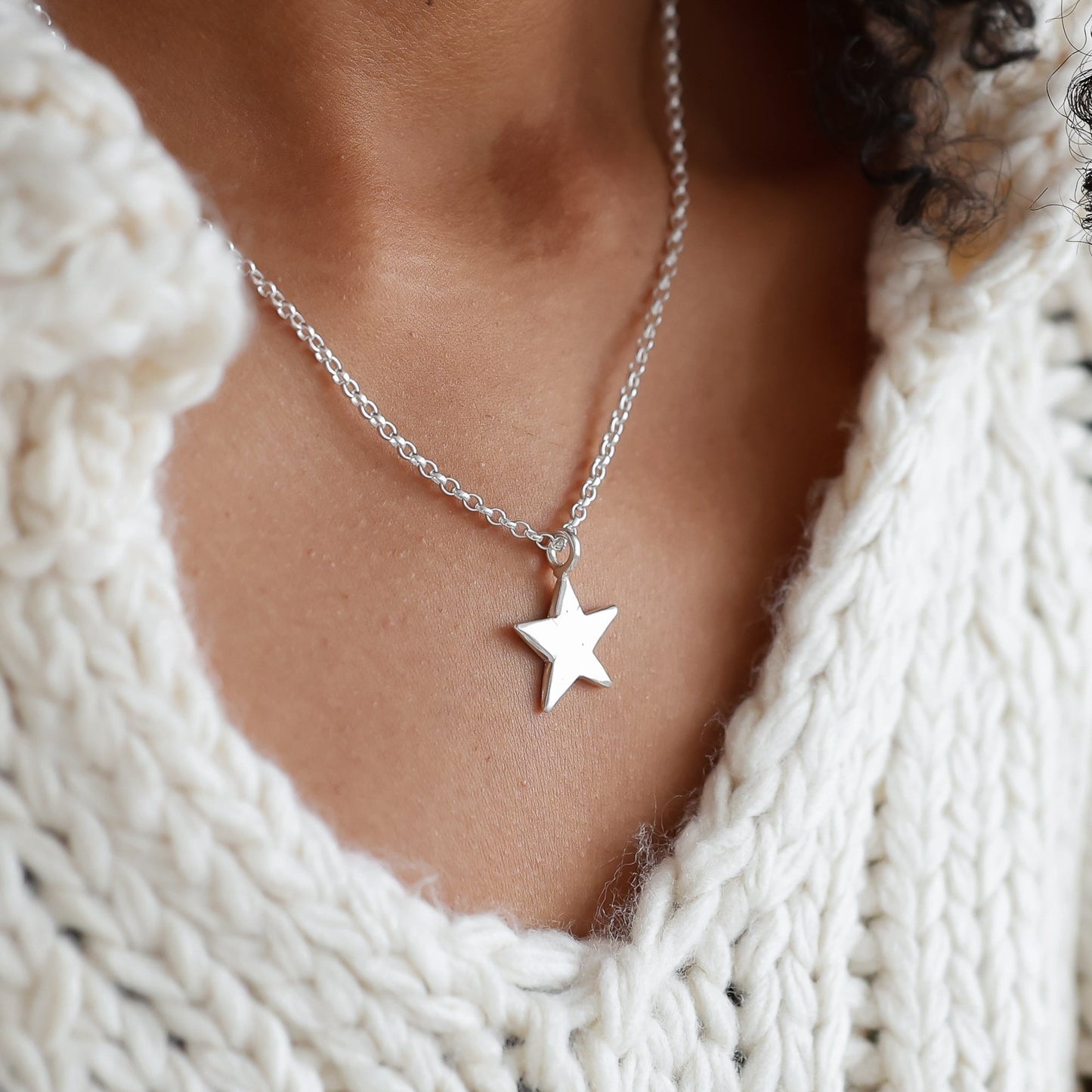 Person wearing a white knitted sweater and star necklace with a blurred background