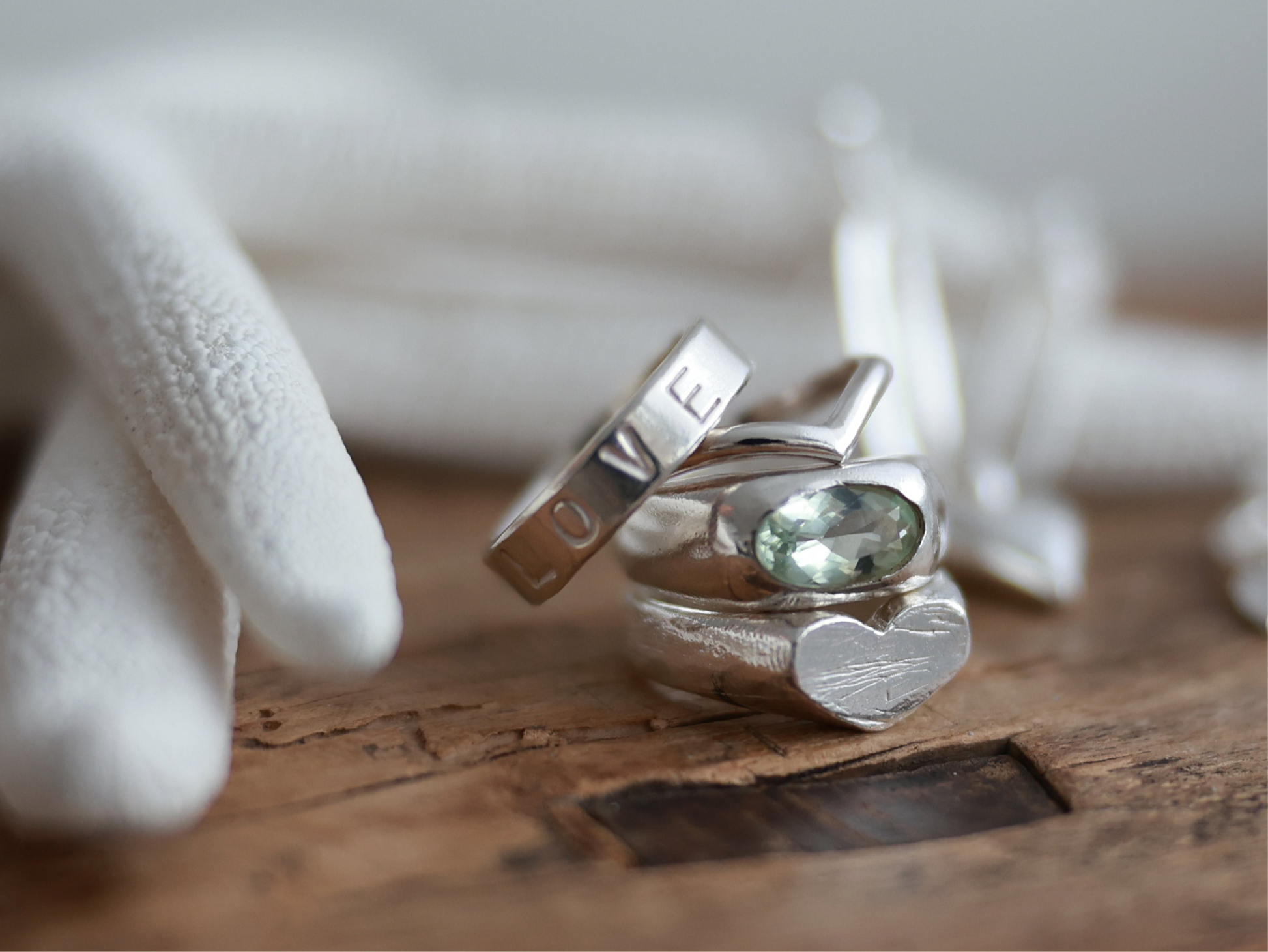 Three silver rings with gemstones on a wooden surface, one ring has 'LOVE' engraved.