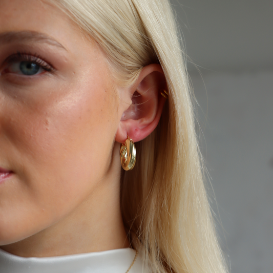 Close-up of elika wearing gold chunky hoop earrings with a neutral background