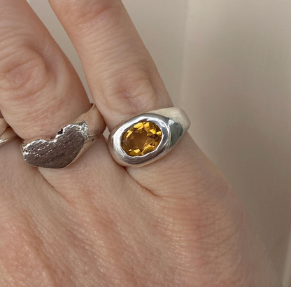 Silver ring with a citrine gemstone on a finger against a neutral background