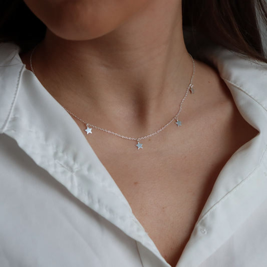 Necklace with star pendants worn by a person against a white shirt background
