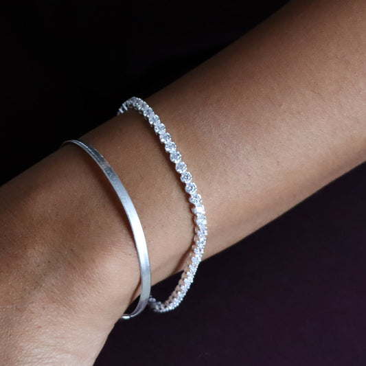 Close-up of a wrist wearing two silver bracelets on a dark background