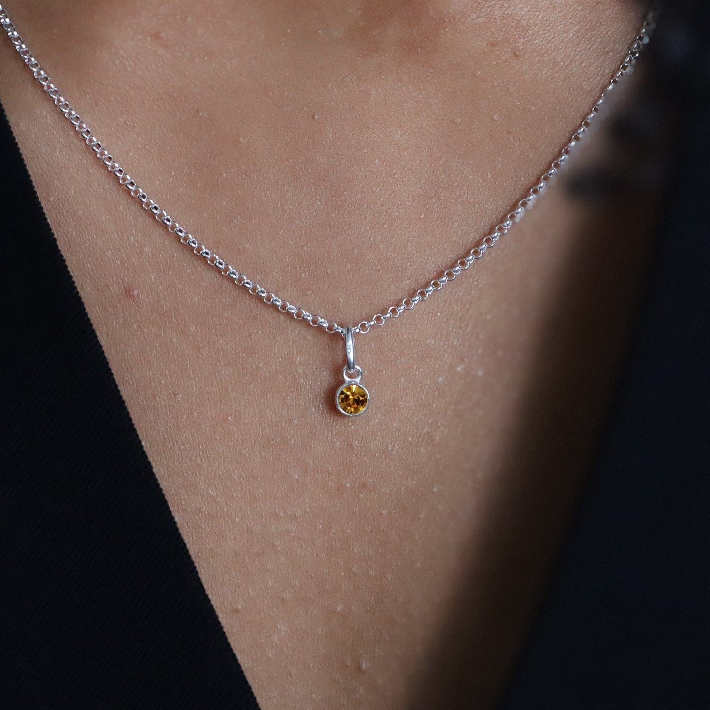 Close-up of a silver necklace with a small pendant worn by a person against a dark background