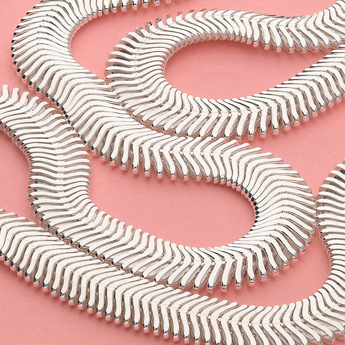 Silver bracelet with wavy design on a pink background