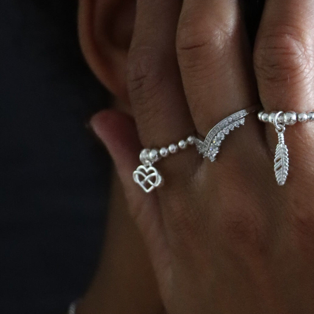 Woman with jewelry on her hand and face, wearing a white top against a dark background