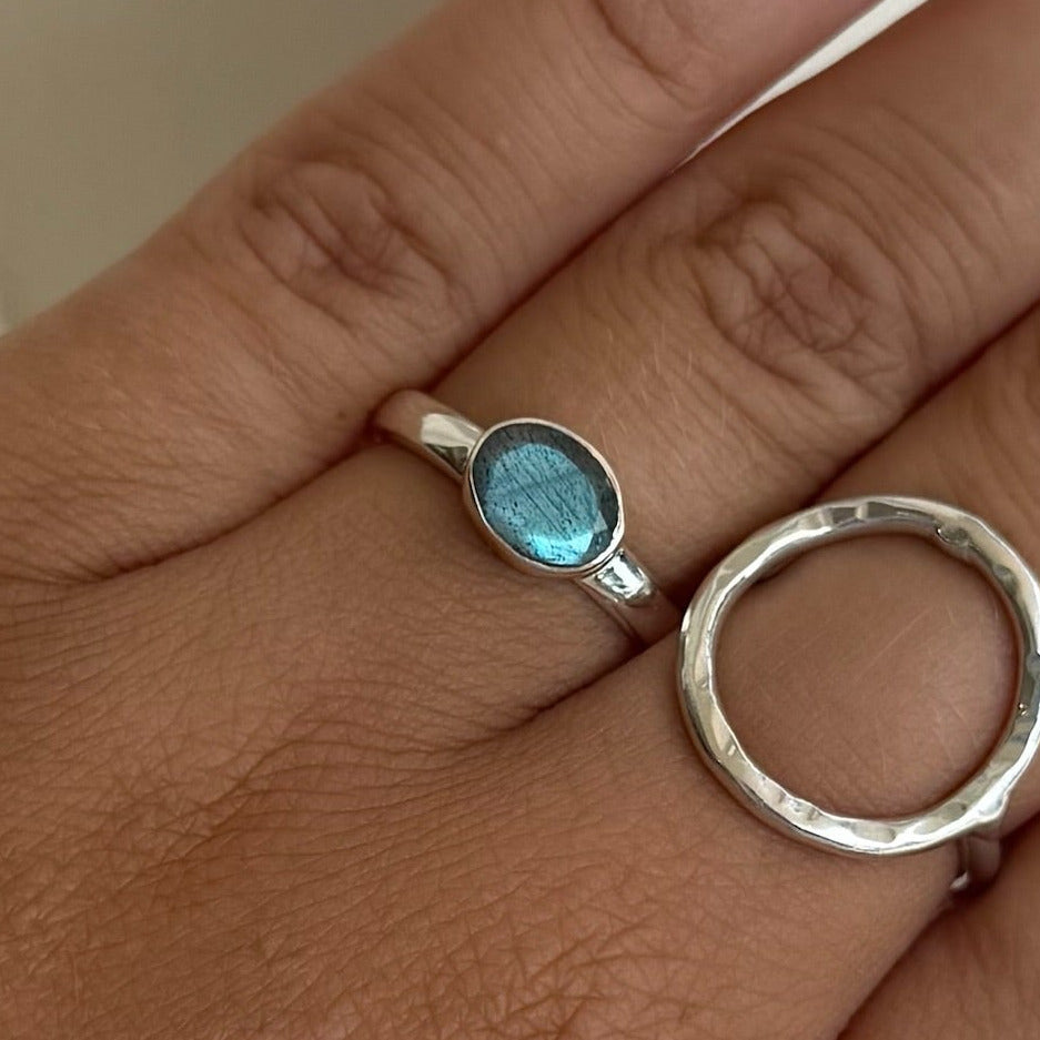 Hand wearing two rings with a blue gemstone and silver band on a neutral background