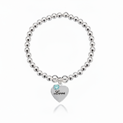 Silver beaded bracelet with a heart-shaped tag and blue gemstone on a white background