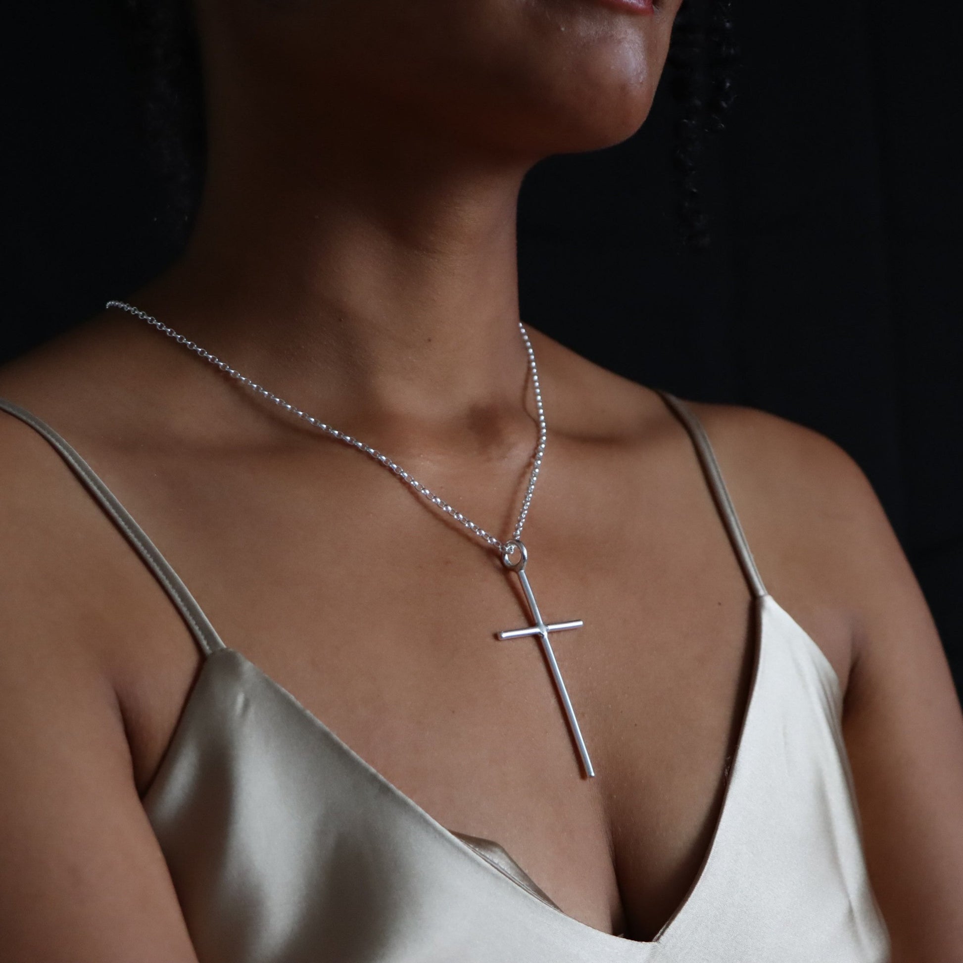 A person wearing a maxi cross necklace with a sterling silver chain and a cross pendant.