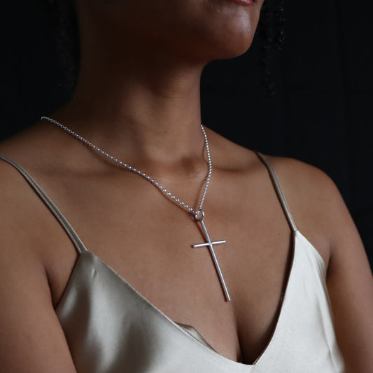 A person wearing a maxi cross necklace with a sterling silver chain and a cross pendant.