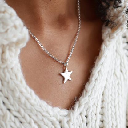 Person wearing a white knitted sweater and star necklace with a blurred background
