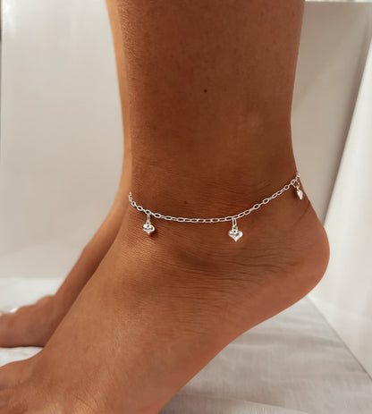 Silver anklet with heart-shaped charms on a person's ankle against a neutral background