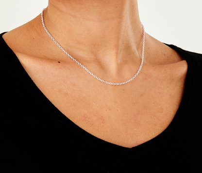 Silver belcher necklace on a person wearing a black top against a white background