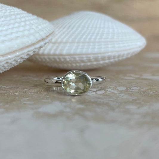 Silver ring with a green gemstone on a wooden surface with shells