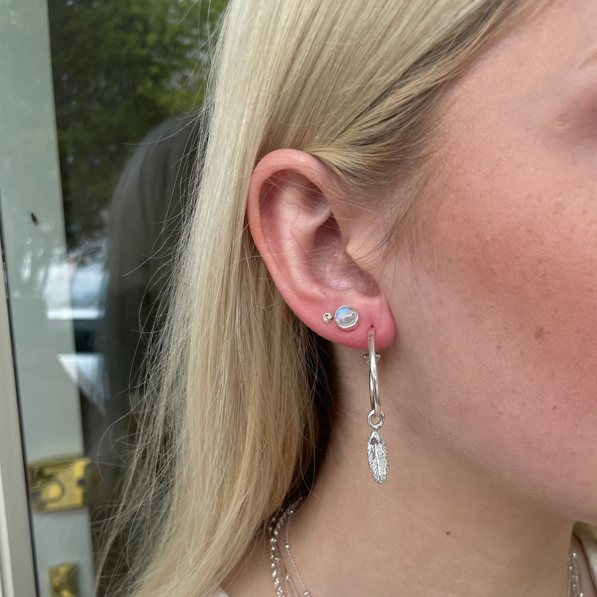 A close-up of a person's ear wearing moonstone studds stacked with other earrings