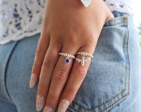 Hand wearing two silver rings with gemstones on a denim background