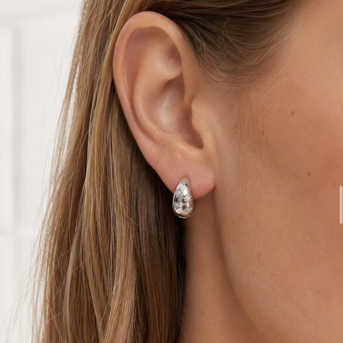Close-up of an ear wearing silver star hoop earrings with a blurred background