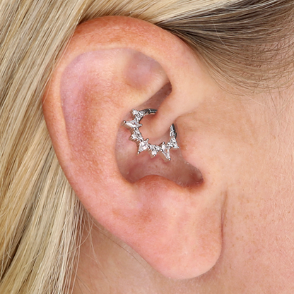 A close-up of a person's ear wearing a silver crescent-shaped ear cuff adorned with small clear rhinestones.