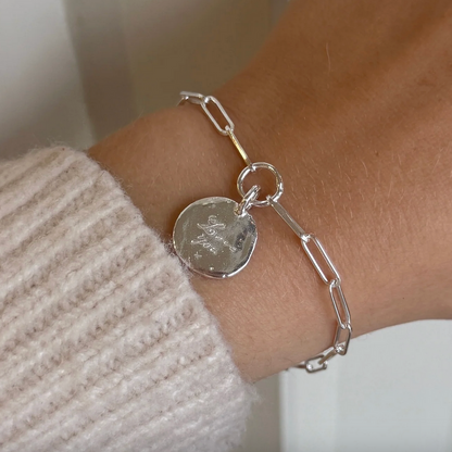 Silver bracelet with a round pendant on a wrist, wearing a beige sweater.