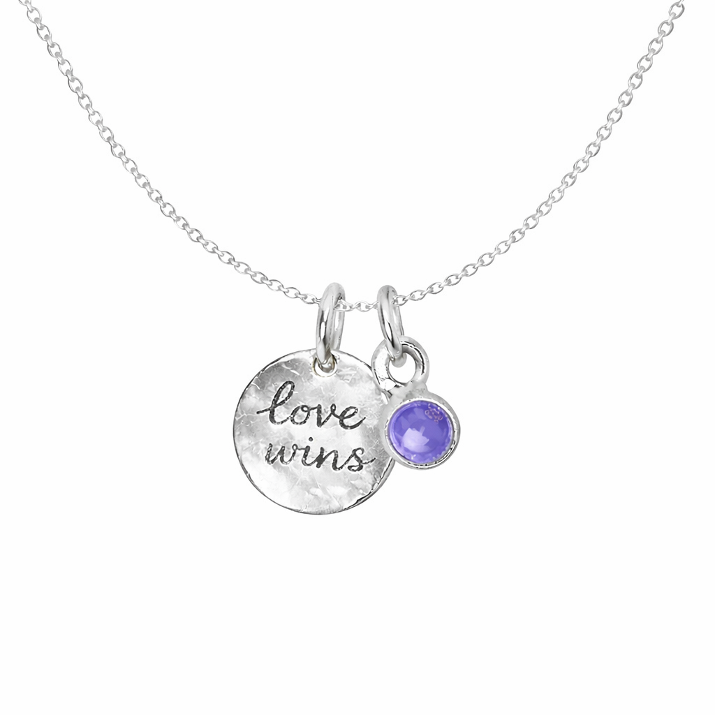 Silver necklace with 'love wins' pendant and tanizanite gemstone on a white background