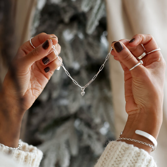 Person holding a delicate silver necklace with a blurred Christmas tree in the background