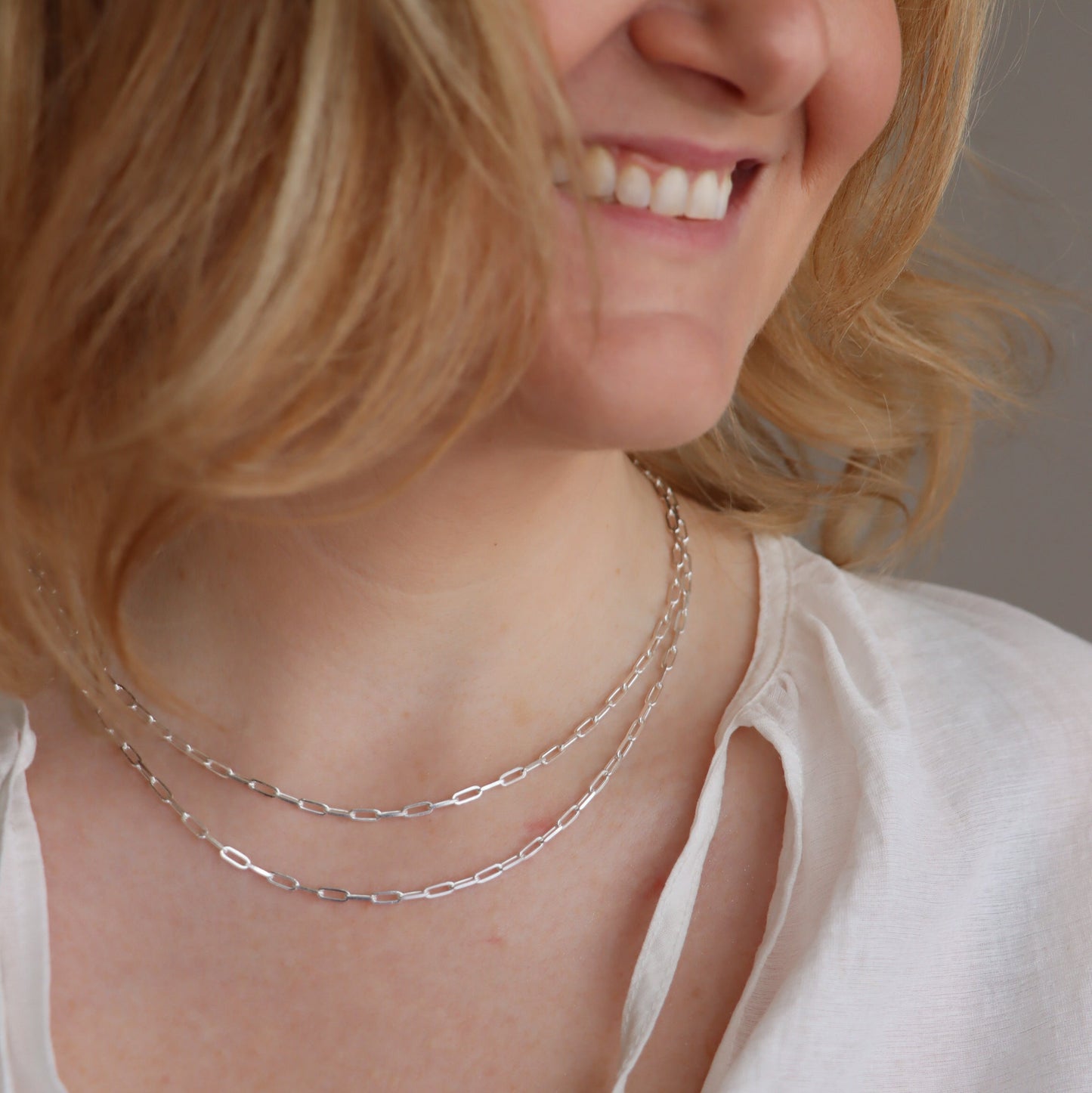 Close-up of a katie wearing a teeny trace necklace with a neutral background