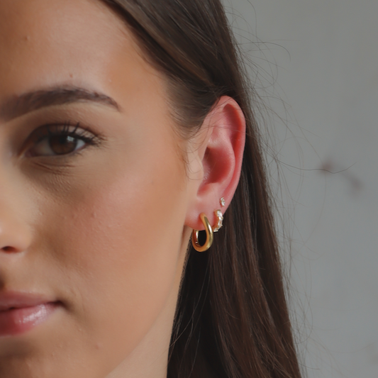 Gold plated wave huggie hoops displayed  on Iyla 