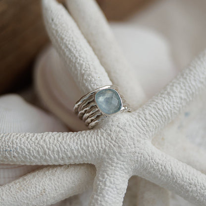 Silver ring with a aquamarine stone on a white starfish against a wooden background