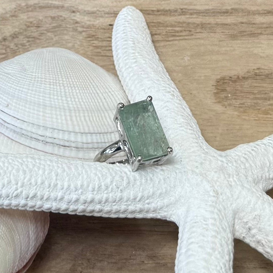 Sterling silver Aquamarine Treasure Ring with a rectangular pale green stone, displayed on a white starfish beside shells.