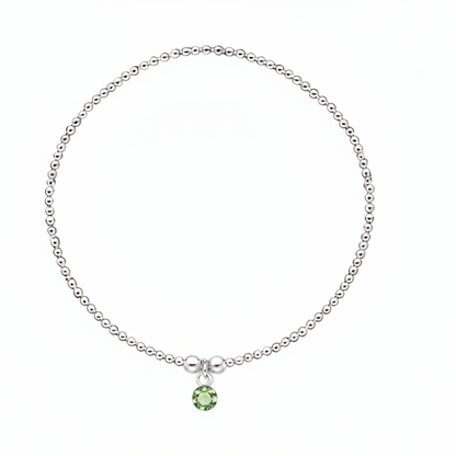 A delicate silver beaded bracelet with a small green gemstone pendant, displayed on a clean white background.