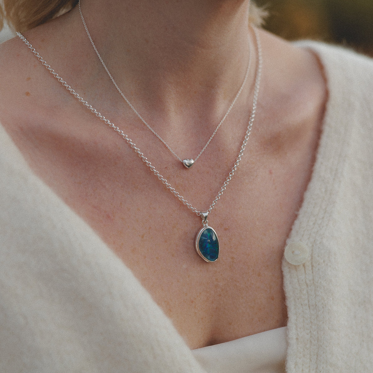 a close up of a person weaing a silver heart necklace with a australian opal layered.