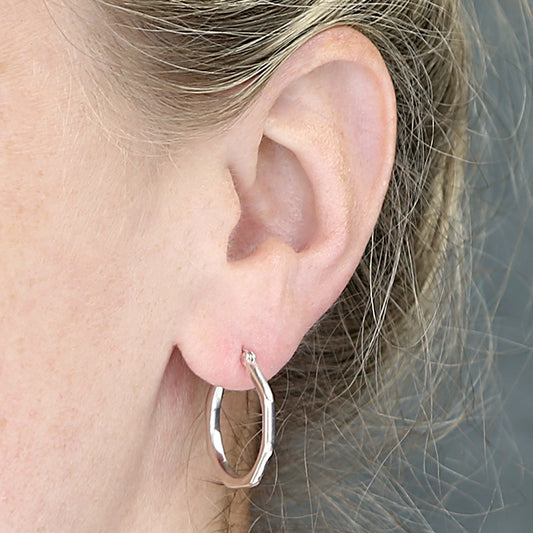 Silver-coloured bamboo-style hoop earring with an angular outline, worn on an ear