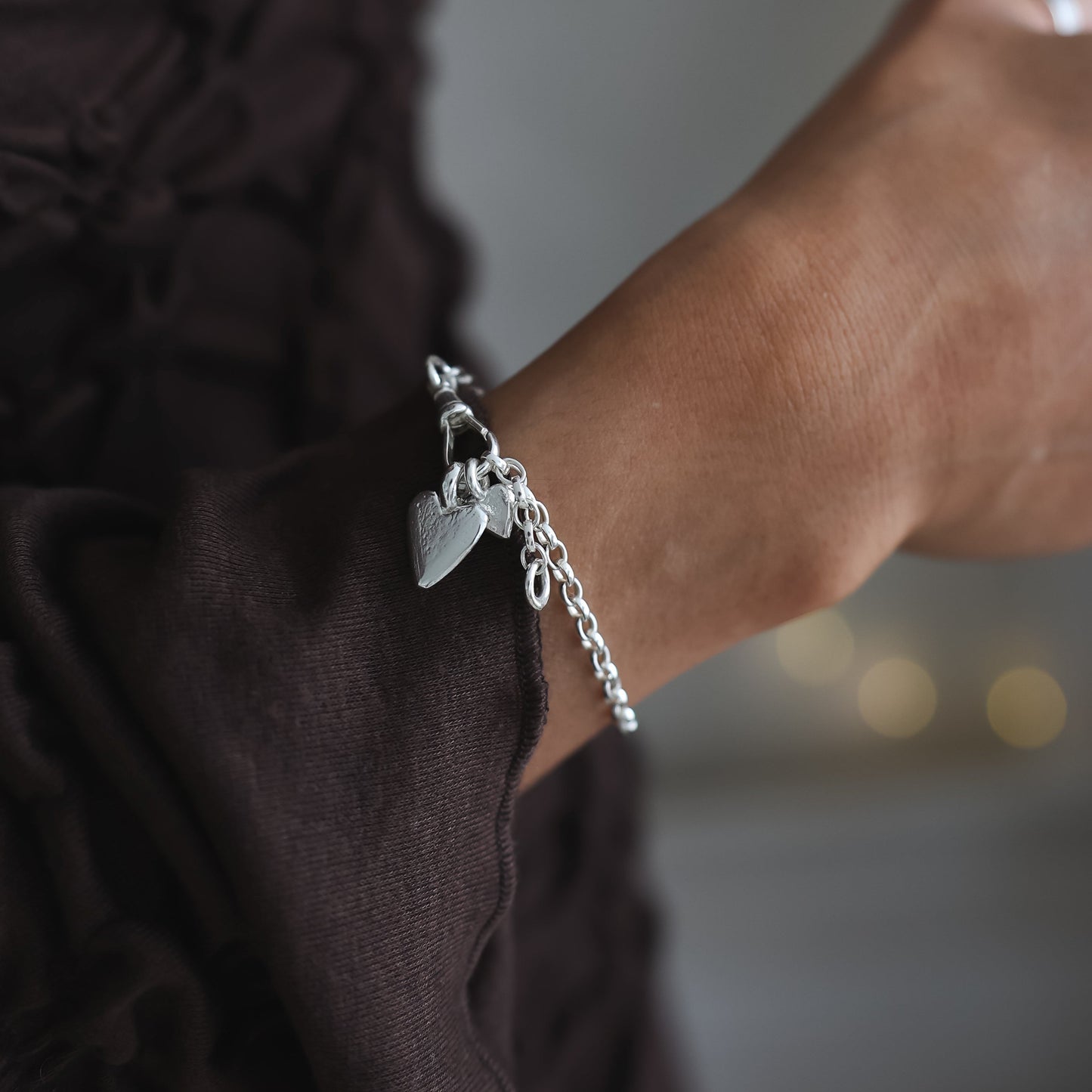 Close-up of a person wearing a silver bracelet with charms against a blurred background