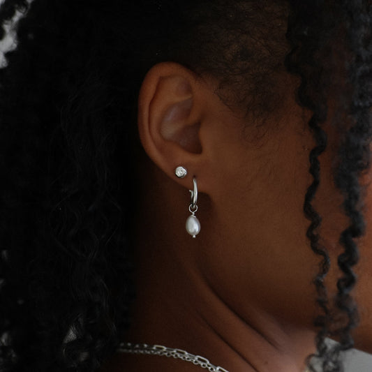 Profile of a young girl with braided hair wearing pearl earrings and a necklace, with a blurred background.