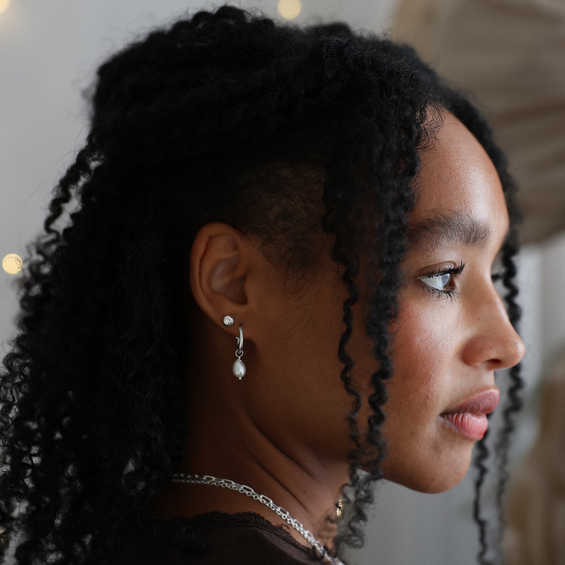 Profile of a young girl with braided hair wearing earrings and a necklace, with a blurred background.