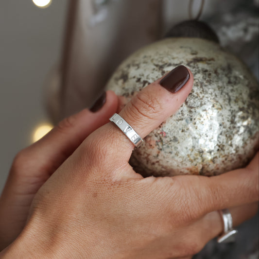 Hand holding a textured silver ornament against a blurred decorative background