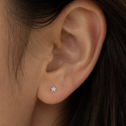 A close-up of a person's ear wearing a small silver star stud earring.