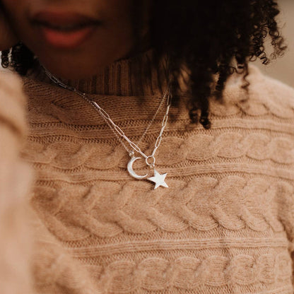 Sterling silver crescent moon necklace layered with a star pendant necklace over a beige knitted jumper.