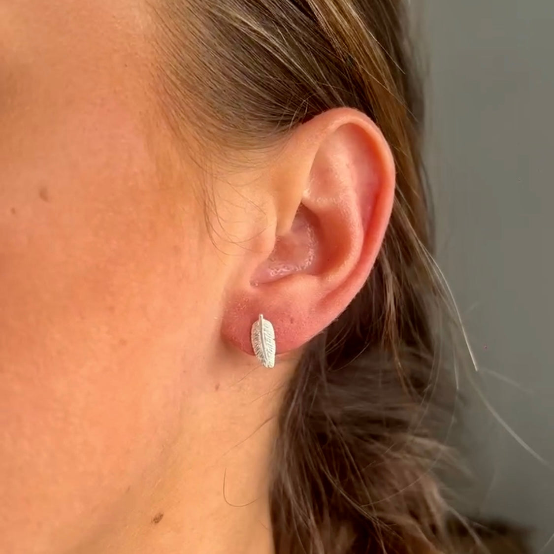 Close-up of an ear wearing a silver earring with a neutral background