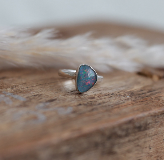 Silver ring with Australian opal stone on a wooden surface