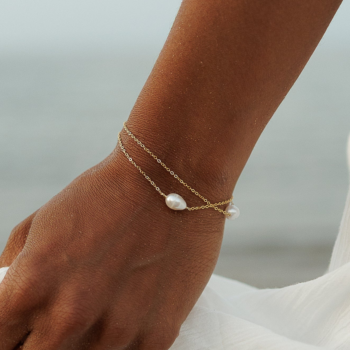 Close-up of a 14ct gold-plated double-chain bracelet with two white pearls, worn on a wrist