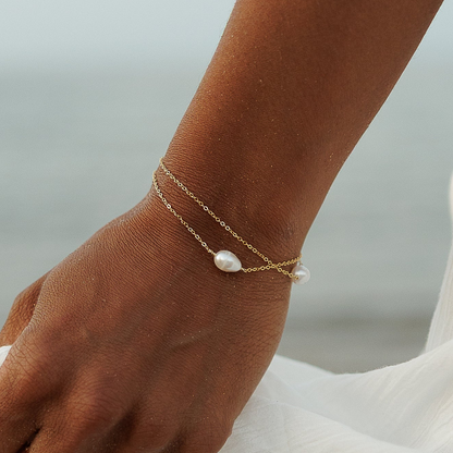Close-up of a 14ct gold-plated double-chain bracelet with two white pearls, worn on a wrist